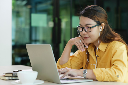 Young woman listening to headphones on laptop in cafe